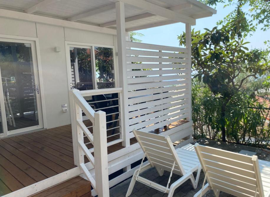 Bright white terrace, relaxing chairs, lush nature, and summer sun.
